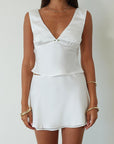 Satin sleeveless crop top. Fixed straps. Front flower detail. Side zipper closure. Back tie closure. Partially lined. white satin tank top. satin tank top. summer top