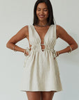 Woven sleeveless dress. Fixed straps. Adjustable drawstring waist. Unlined. tan mini dress. cream mini dress. summer dress. dinner dress. evening dress. vacation dress. vacation outfit