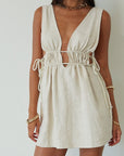 Woven sleeveless dress. Fixed straps. Adjustable drawstring waist. Unlined. tan mini dress. cream mini dress. summer dress. dinner dress. evening dress. vacation dress. vacation outfit