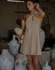 Woven dress. Adjustable halter neckline with tie closure. Back hook and eye and zipper closures. Fully lined. European summer. European summer dress. European summer aesthetic. Tuscany outfit inso. Tuscany aesthetic. Summer dress. oat mini dress. beige mini dress. tan mini dress. mini halter neck dress. summer outfit. everyday dress. vacation dress. outfit to wear to tuscany. nice dinner dress. dinner dress. day dress.