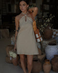 Woven dress. Adjustable halter neckline with tie closure. Back hook and eye and zipper closures. Fully lined. European summer. European summer dress. European summer aesthetic. Tuscany outfit inso. Tuscany aesthetic. Summer dress. oat mini dress. beige mini dress. tan mini dress. mini halter neck dress. summer outfit. everyday dress. vacation dress. outfit to wear to tuscany. nice dinner dress. dinner dress. day dress.