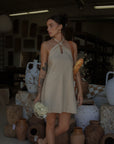 Woven dress. Adjustable halter neckline with tie closure. Back hook and eye and zipper closures. Fully lined. European summer. European summer dress. European summer aesthetic. Tuscany outfit inso. Tuscany aesthetic. Summer dress. oat mini dress. beige mini dress. tan mini dress. mini halter neck dress. summer outfit. everyday dress. vacation dress. outfit to wear to tuscany. nice dinner dress. dinner dress. day dress.