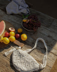 Woven macrame crossbody bag. Fixed strap. Fringe trim. Front zipper closure. Fully lined.