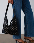 Studded vegan leather bag. Fixed top strap. Top snap button closure. Fully lined. Inner pockets and zipper pocket.