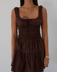 Smocked woven dress. Elastic straps. Front tie closure. Elastic waist. Side pockets. Fully lined. brown mini dress. fall transition dress