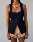 Denim sleeveless top. Fixed straps. Front button down closures. Faux front pockets. Adjustable back tie closure. Unlined. denim vest
