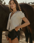 Woven top. Collar neckline. Short sleeves with elastic sleeve openings. Front tie closure. Unlined. coquette cream top