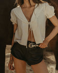 Woven top. Collar neckline. Short sleeves with elastic sleeve openings. Front tie closure. Unlined. coquette cream top