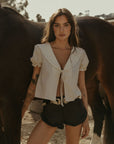 Woven top. Collar neckline. Short sleeves with elastic sleeve openings. Front tie closure. Unlined. coquette cream top