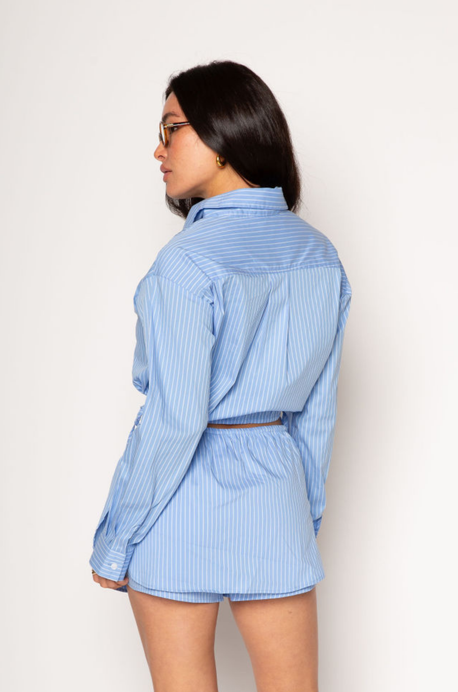 Striped woven cropped shirt. Collar neckline. Long sleeves with button closures. Front button down closures. Drawstring side ties. Unlined. blue stripe crop top. studious oufit