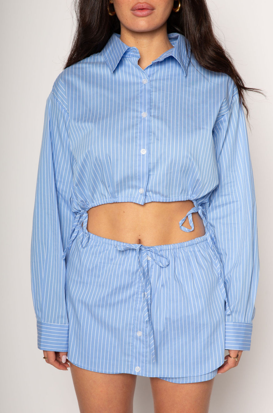 Striped woven cropped shirt. Collar neckline. Long sleeves with button closures. Front button down closures. Drawstring side ties. Unlined. blue stripe crop top. studious oufit