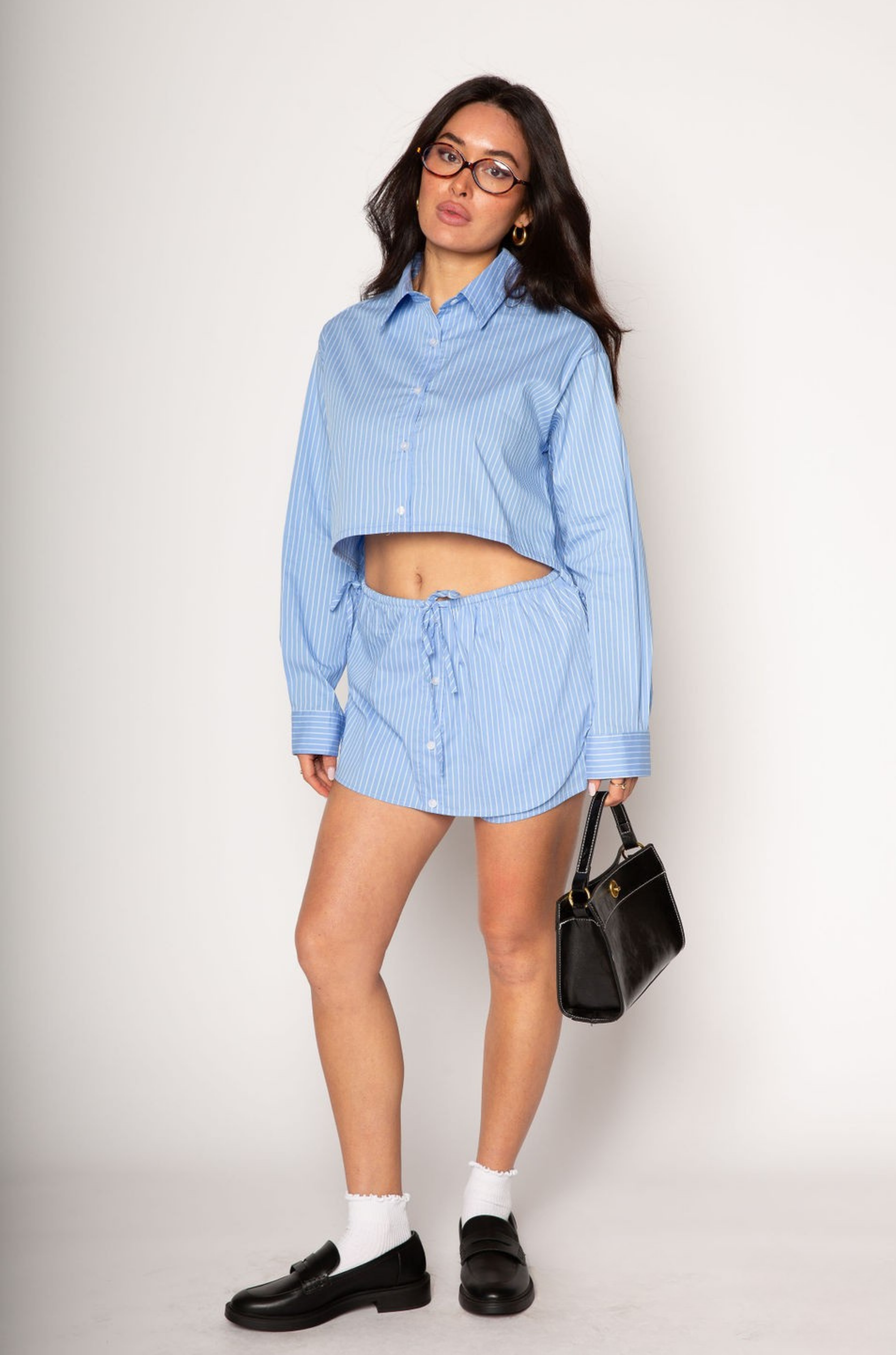 Striped woven cropped shirt. Collar neckline. Long sleeves with button closures. Front button down closures. Drawstring side ties. Unlined. blue stripe crop top. studious oufit