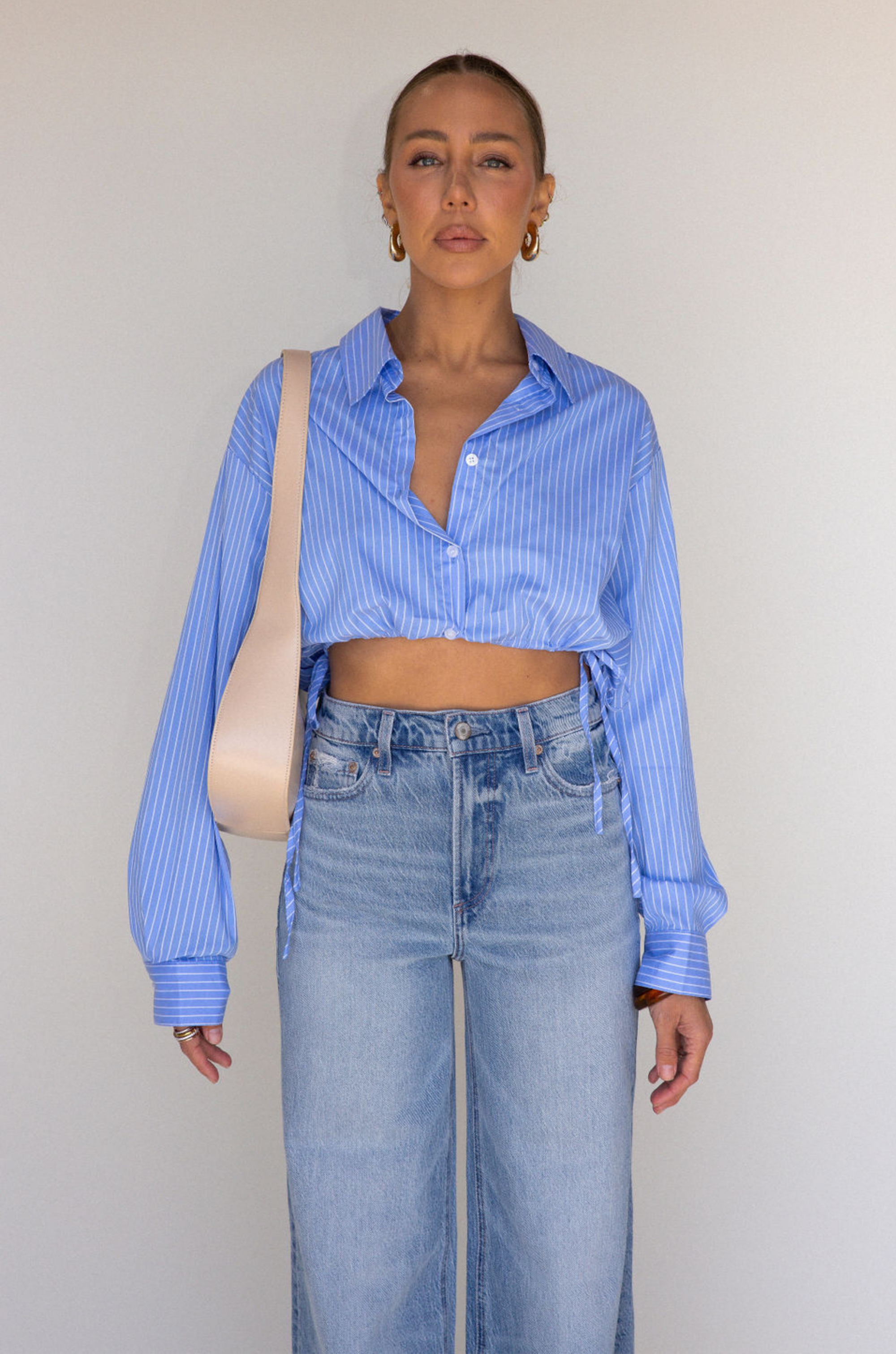Striped woven cropped shirt. Collar neckline. Long sleeves with button closures. Front button down closures. Drawstring side ties. Unlined. blue stripe crop top. studious oufit