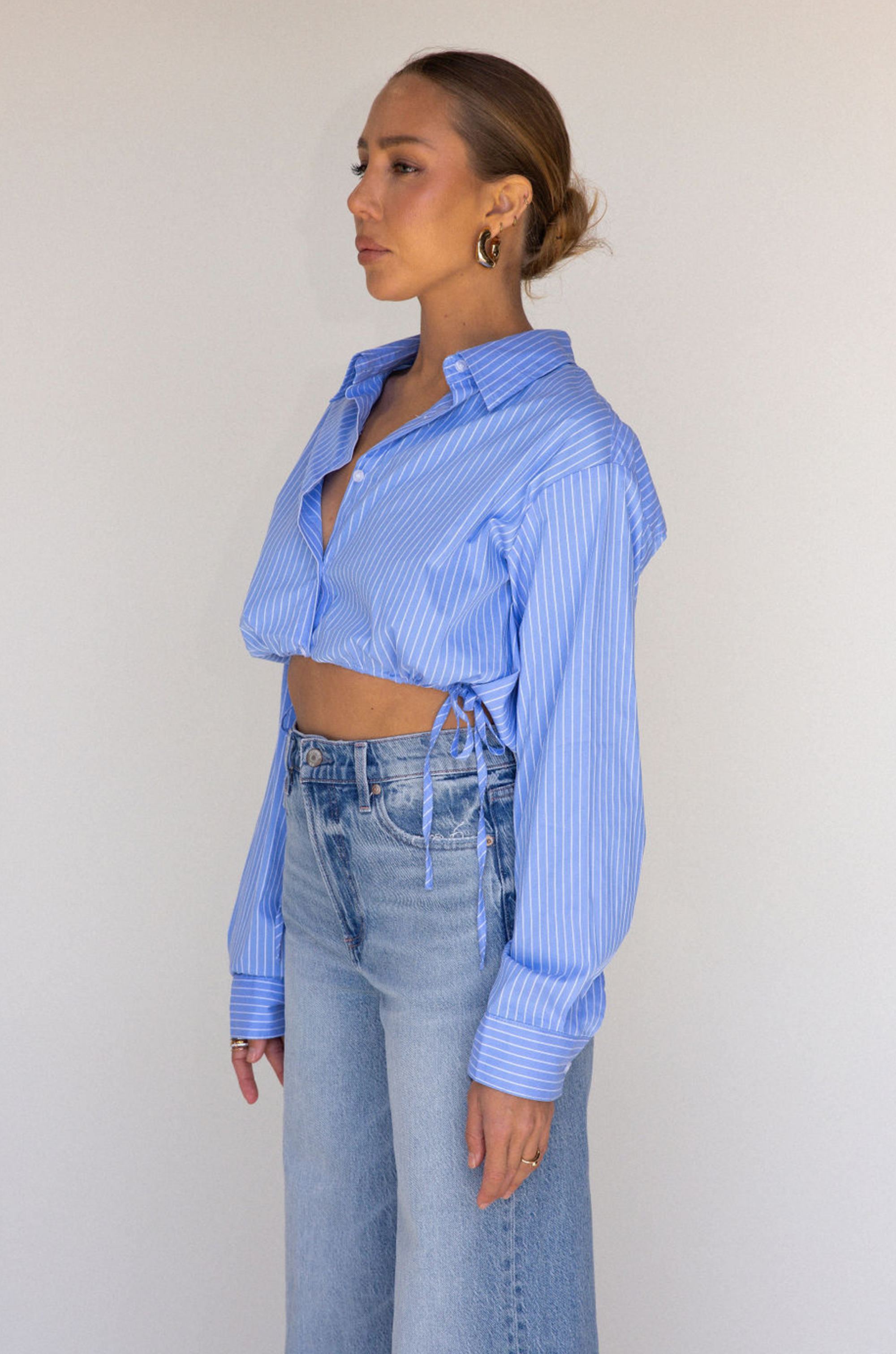 Striped woven cropped shirt. Collar neckline. Long sleeves with button closures. Front button down closures. Drawstring side ties. Unlined. blue stripe crop top. studious oufit