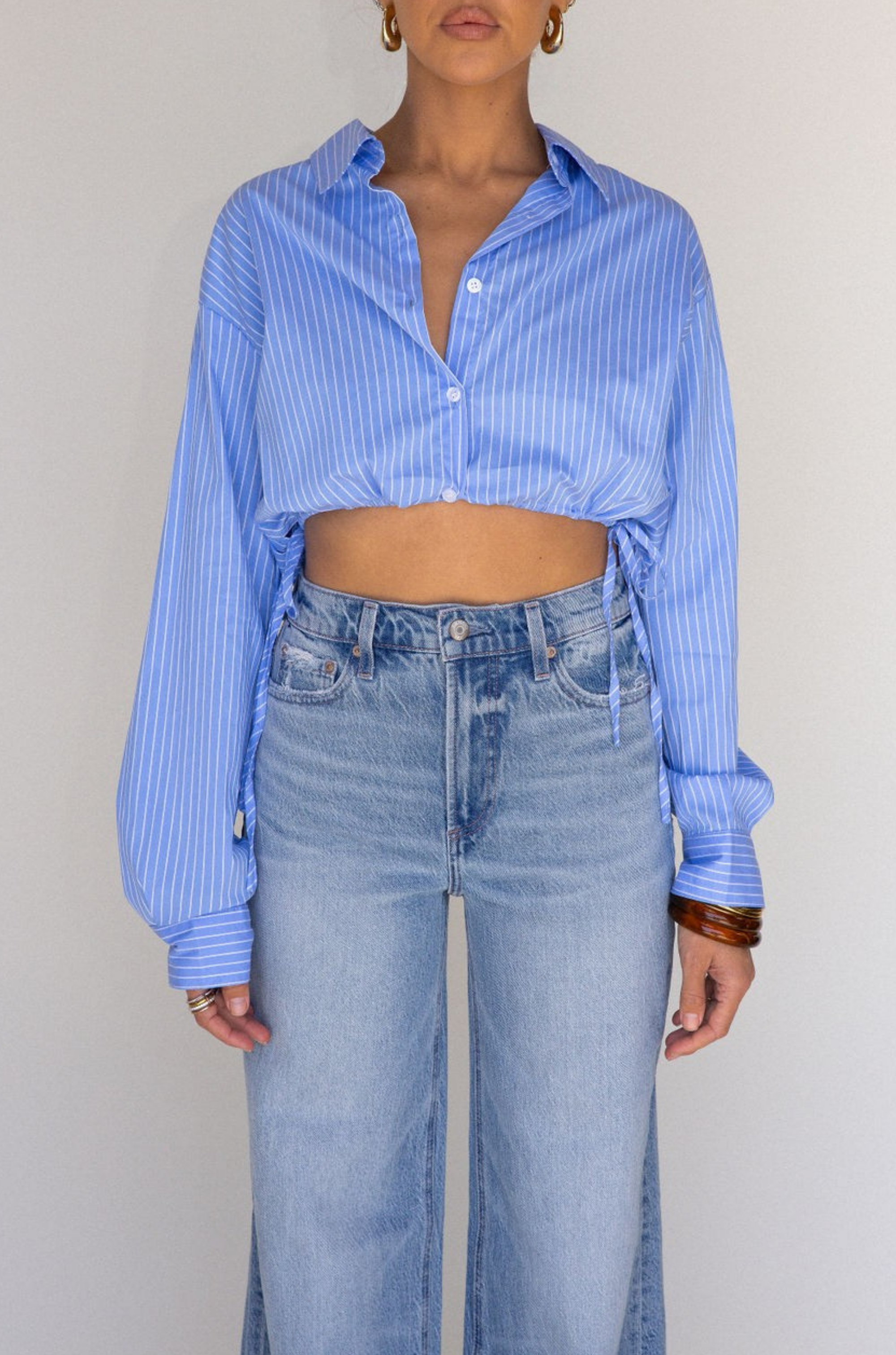 Striped woven cropped shirt. Collar neckline. Long sleeves with button closures. Front button down closures. Drawstring side ties. Unlined. blue stripe crop top. studious oufit