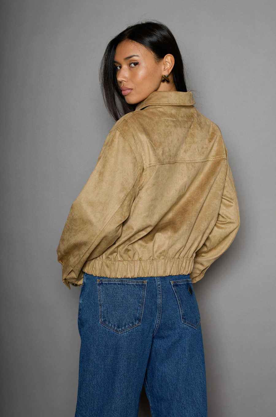 Vegan suede bomber jacket. Collar neckline. Front zipper closure. Elastic hems. Front pockets with snap button closures. Fully lined. tan suede bomber