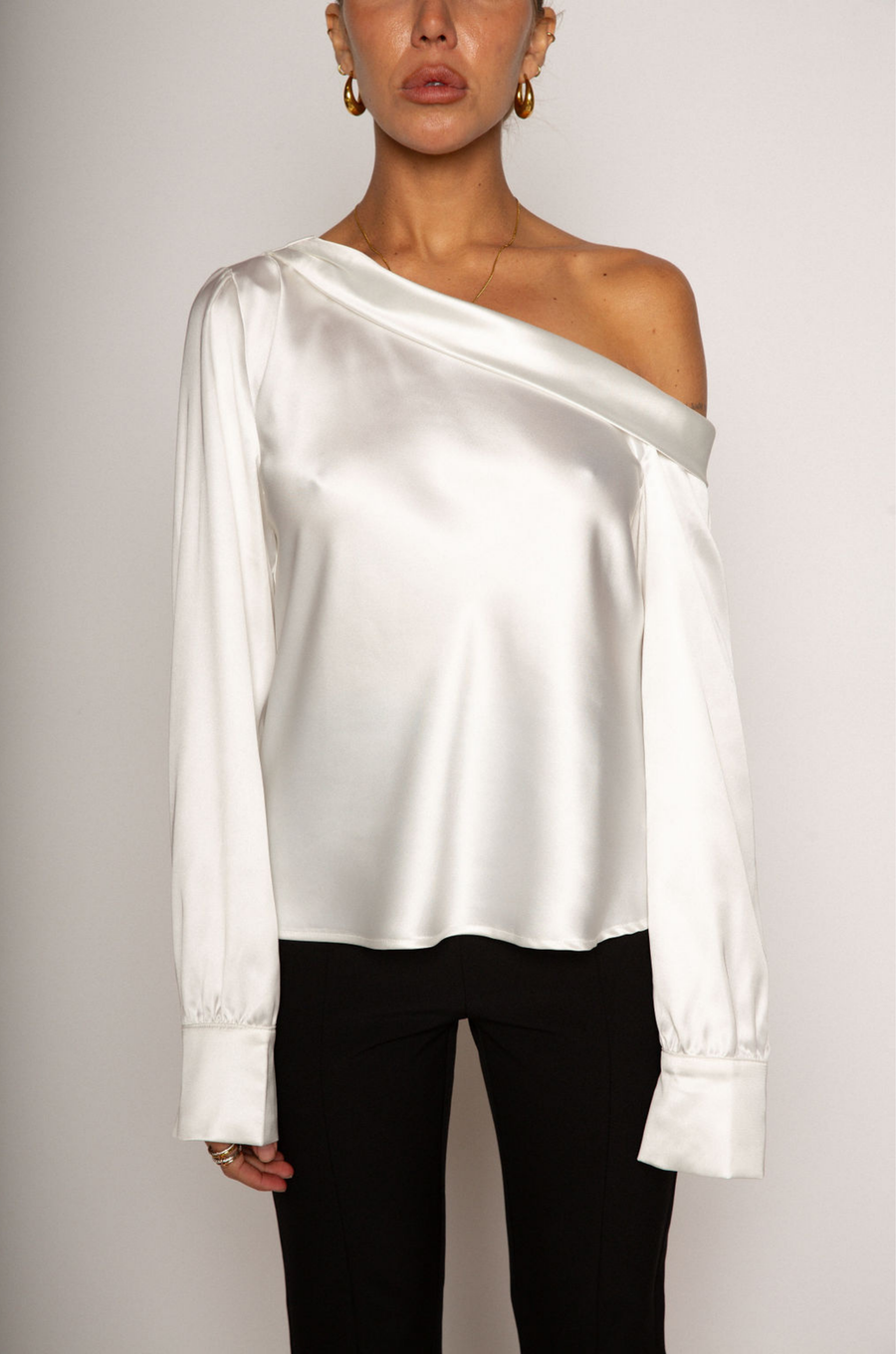 white Satin top. Folded off the shoulder neckline. Long sleeves with button closures. Unlined. white satin one shoulder top. 