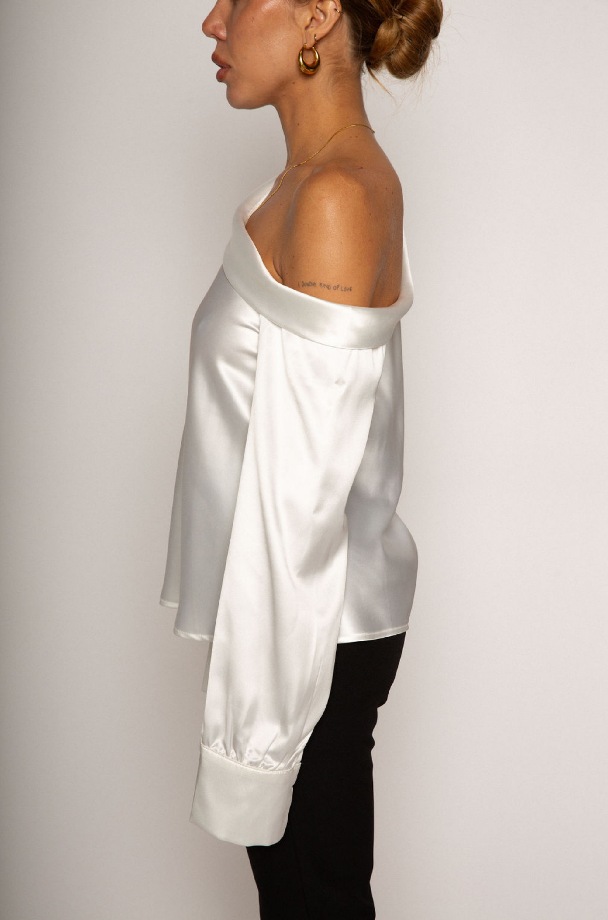 white Satin top. Folded off the shoulder neckline. Long sleeves with button closures. Unlined. white satin one shoulder top. 