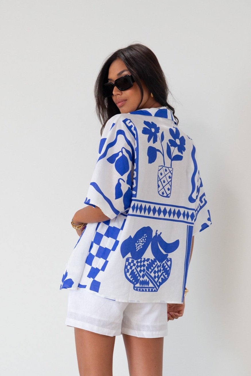 Printed woven shirt. Collar neckline. Short sleeves. Front button down closure. Unlined. cover up shirt. button up cover up. blue and white printed shirt. summer top. beach cover up. pool coverup