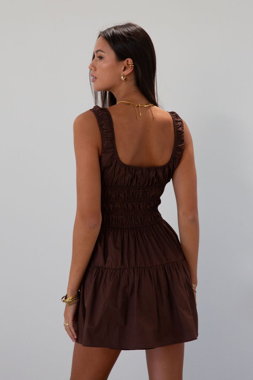 Smocked woven dress. Elastic straps. Front tie closure. Elastic waist. Side pockets. Fully lined. brown mini dress. fall transition dress