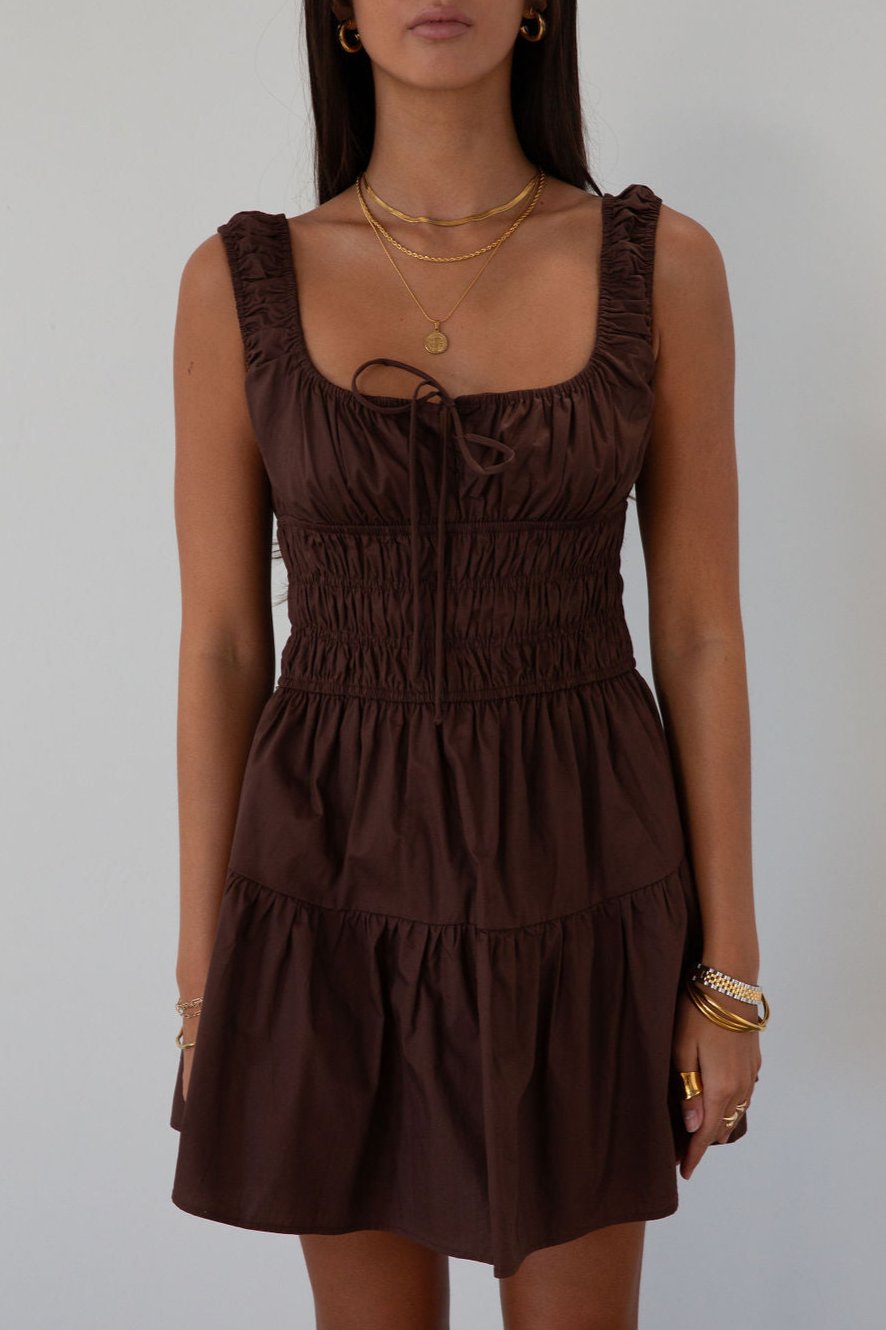 Smocked woven dress. Elastic straps. Front tie closure. Elastic waist. Side pockets. Fully lined. brown mini dress. fall transition dress