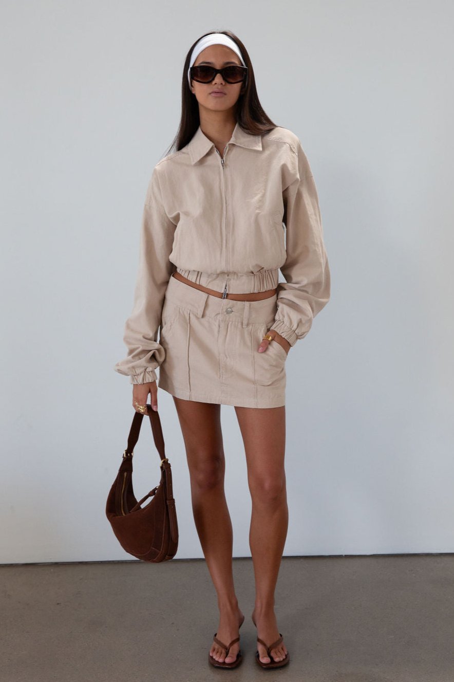 Denim cropped jacket. Collar neckline. Front zipper closure. Elastic hem. Long sleeves with elastic openings. Faux front pockets. Unlined. tan denim jacket. bomber jacket. cream bomber jacket. fall outfit