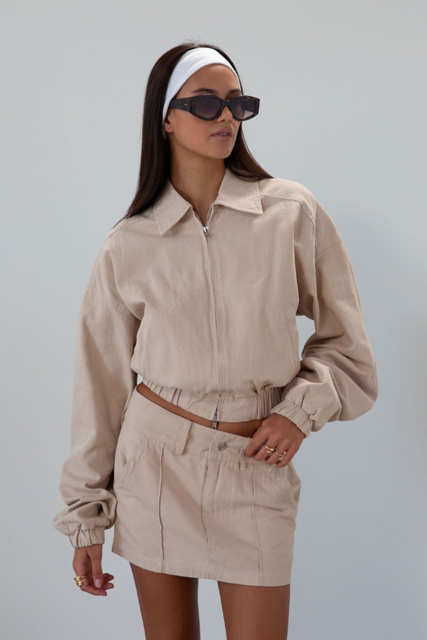 Denim cropped jacket. Collar neckline. Front zipper closure. Elastic hem. Long sleeves with elastic openings. Faux front pockets. Unlined. tan denim jacket. bomber jacket. cream bomber jacket. fall outfit