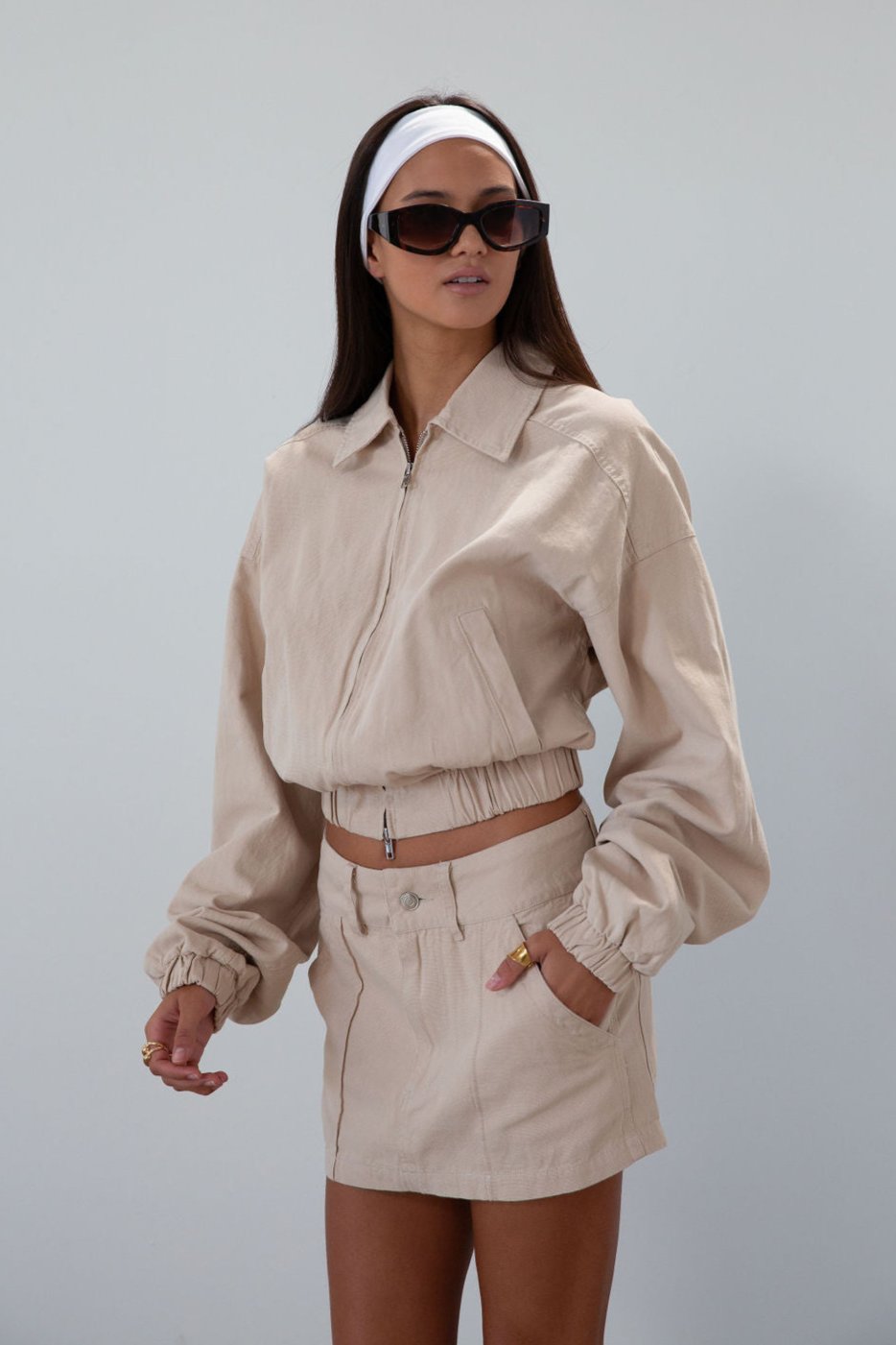 Denim cropped jacket. Collar neckline. Front zipper closure. Elastic hem. Long sleeves with elastic openings. Faux front pockets. Unlined. tan denim jacket. bomber jacket. cream bomber jacket. fall outfit