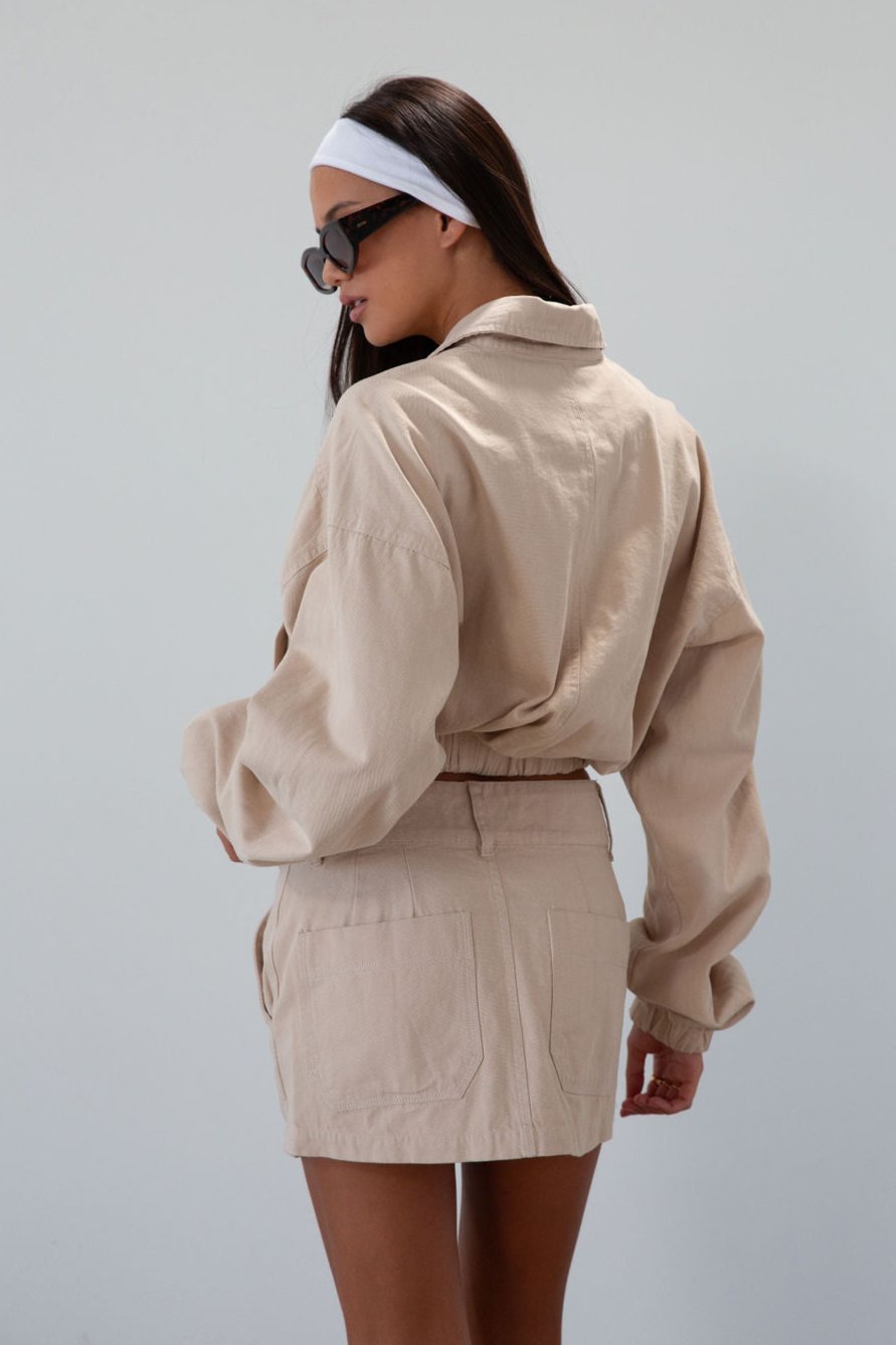 Denim cropped jacket. Collar neckline. Front zipper closure. Elastic hem. Long sleeves with elastic openings. Faux front pockets. Unlined. tan denim jacket. bomber jacket. cream bomber jacket. fall outfit