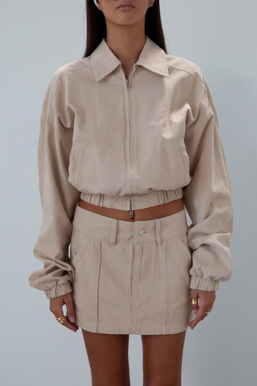 Denim cropped jacket. Collar neckline. Front zipper closure. Elastic hem. Long sleeves with elastic openings. Faux front pockets. Unlined. tan denim jacket. bomber jacket. cream bomber jacket. fall outfit