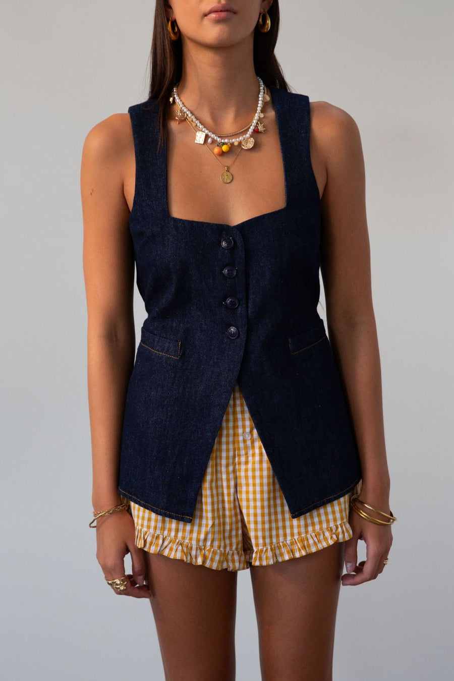 Denim sleeveless top. Fixed straps. Front button down closures. Faux front pockets. Adjustable back tie closure. Unlined. denim vest