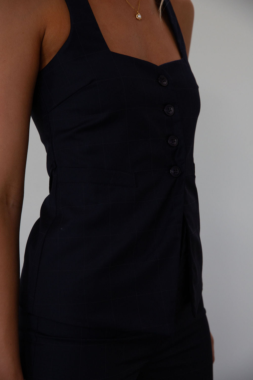 Plaid woven sleeveless top. Front button down closure. Faux front pockets. Adjustable back tie closure. Fully lined. navy blue blouse. work outfit. business casual outfit. 
