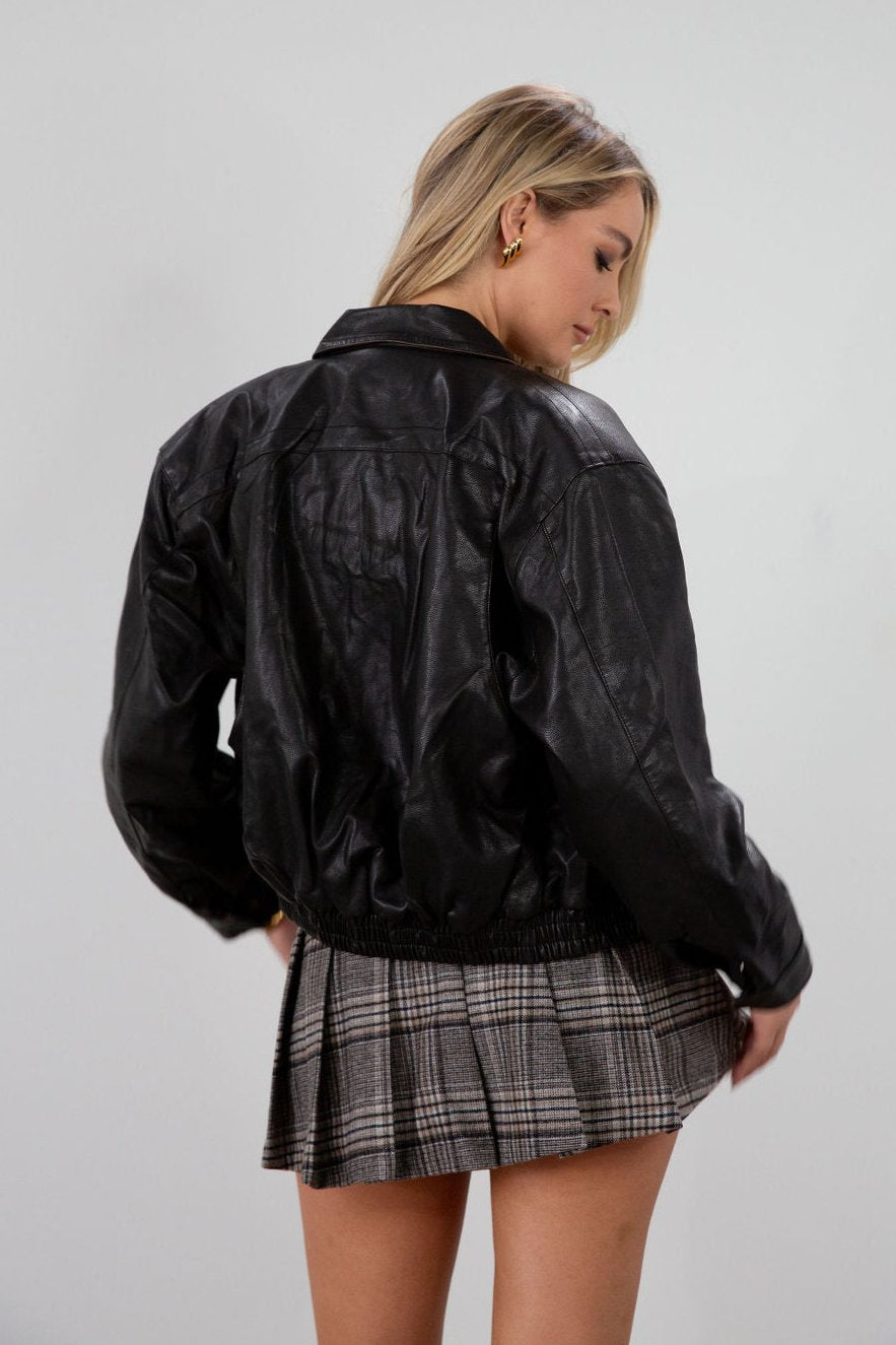 Vegan leather bomber jacket. Collar neckline. Long sleeves with snap button closures. Front snap button and zipper closures. Front pockets. Elastic hem. Fully lined. dark brown faux leather bomber jacket. fall jacket. bomber jacket