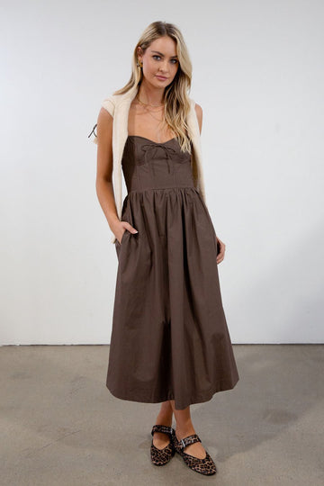 Woven midi dress. Adjustable tie straps. Front tie closure. Side pockets. Elastic smocked back panel. Back hook and eye and zipper closures. Unlined. brown midi dress. fall dress. cute fall dress